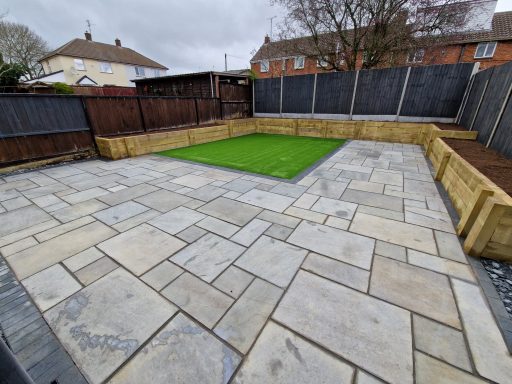 A grey Indian sandstone patio with timber planters and grass area